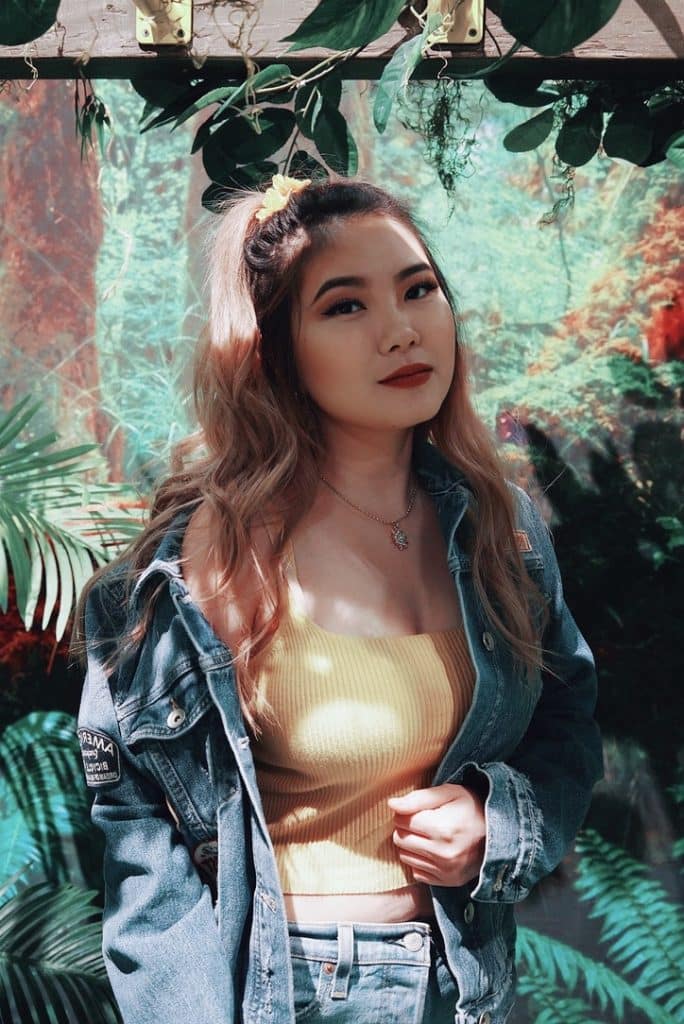 blonde girl in jungle theme background in yellow top with jean jacket and sunflower hairband