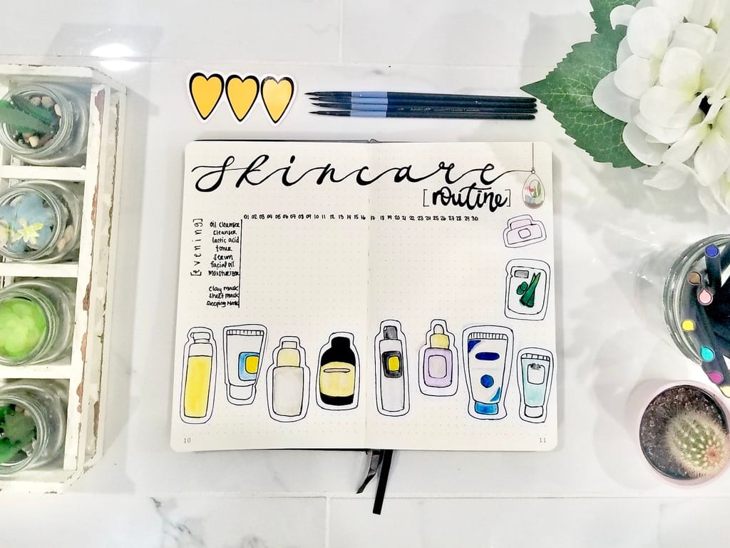 bullet journal for skincare routine surrounded by succulent plants and jar of markers and flowers