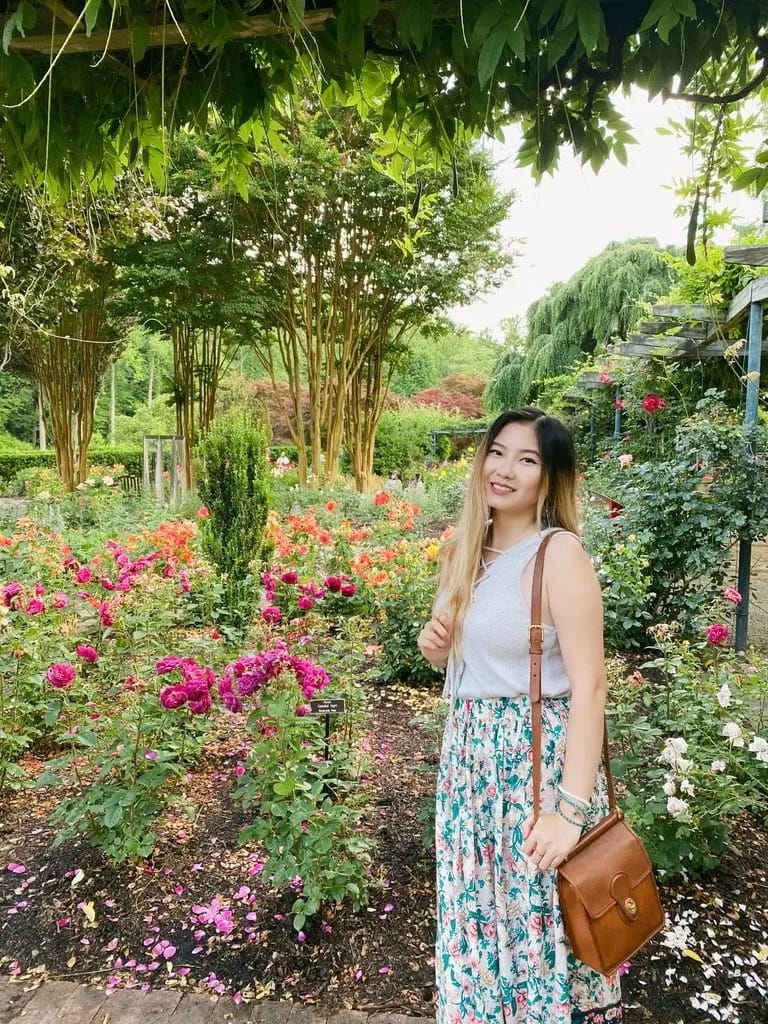 blonde asian girl standing in field of pink and orange roses and trees at brookside gardens maryland